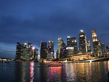 Illuminated buildings by river against sky at night