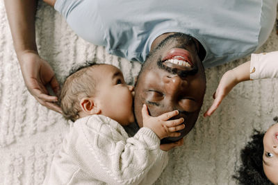 Baby boy kissing father lying on blanket at home