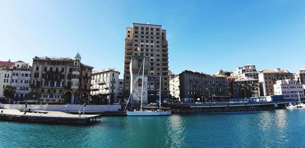 View of buildings by river against blue sky