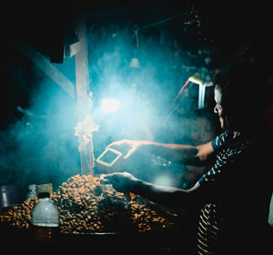 Man selling food at illuminated stall during night