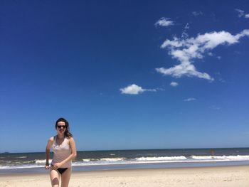 Smiling woman running on shore at beach against sky