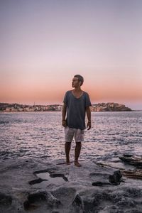 Young man standing on beach against sky during sunset