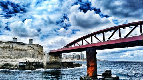 Low angle view of bridge over sea against cloudy sky
