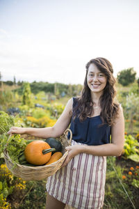 Portrait of happy woman carrying vegetables in basket against clear sky at community garden