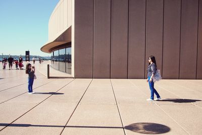 People walking on footpath in city against sky
