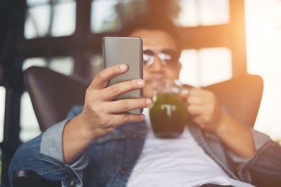 Young man using smart phone while drinking juice at cafe