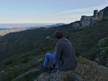 Rear view of man sitting on rock against mountain