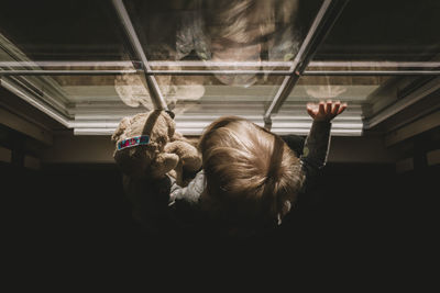 Girl with teddy bear by window at home