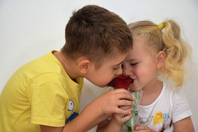 Close-up of siblings smelling red rose against wall
