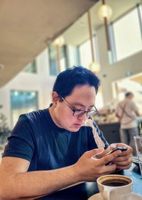 Side view of young asian man using smartphone while drinking coffee in a cafe.