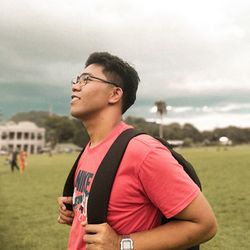 Portrait of young man standing on field against sky