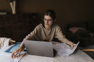 Non-binary person collecting bills while sitting with laptop at home