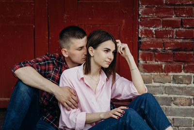 Man romancing with woman while sitting against house