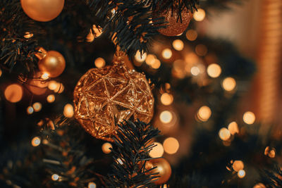 Golden shiny christmas ball hanging on a christmas tree with golden garland lights. 