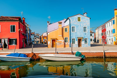 Boats moored in canal by buildings against clear sky