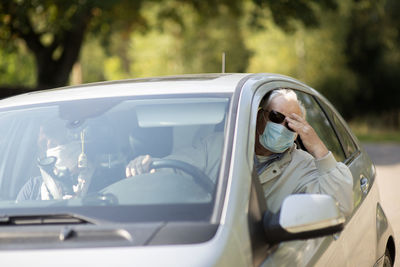 Senior couple wearing anti virus masks are driving in a car during the covid-19 pandemic