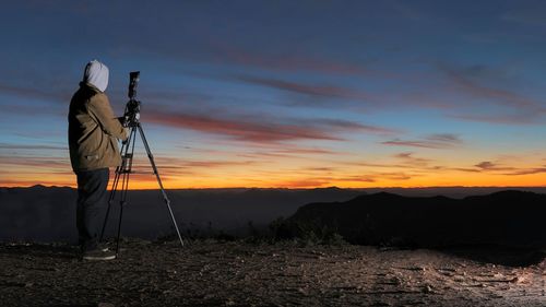 Man photographing on landscape against sky during sunset