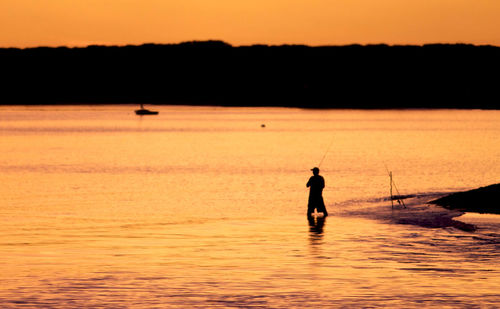 Rear view of silhouette man fishing in lake at sunset