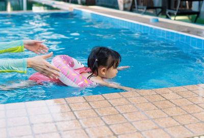 Cropped hands of woman with daughter swimming in pool