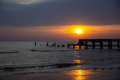 Silhouette wooden posts on beach against sky during sunset