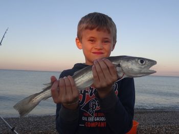Portrait of boy holding fish at beach during sunset