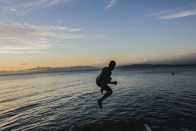Silhouette boy jumping over sea against sky