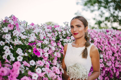 Portrait of bride standing by pink flowers against sky