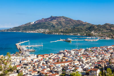 Aerial view of cityscape by sea against blue sky