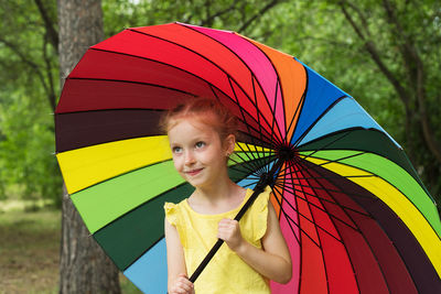 Happy funny girl holding rainbow umbrella. cute happy schoolgirl playing in rainy summer park. 