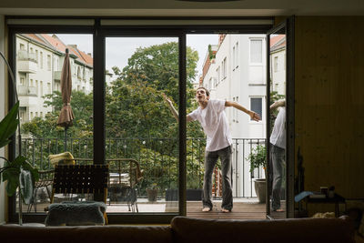 Carefree man dancing in balcony seen through door