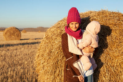 Portrait of a beautiful young model in knitted hat and warm clothes with little baby play, enjoy day