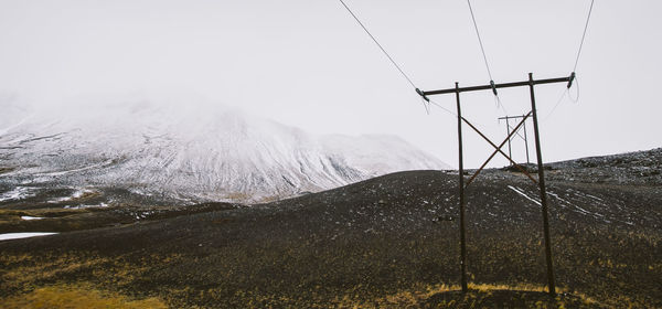 Electricity pylon on snowcapped mountain against sky