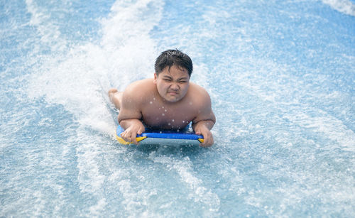 Obese boy play wave machine on surfboard, recreation and sport concept