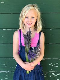 Portrait of cute girl standing with plants against wooden wall