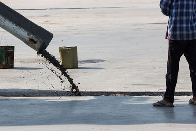 Low section of man standing by concrete pouring on road in city