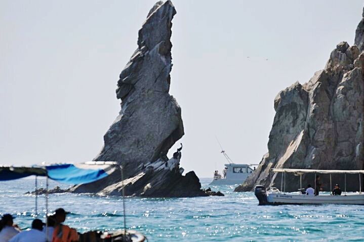 nautical vessel, sea, water, clear sky, transportation, boat, mode of transport, rock formation, rock - object, mountain, travel, sailboat, copy space, men, tourism, nature, cliff, scenics, day