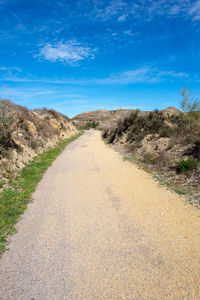 Dirt road amidst landscape against blue sky