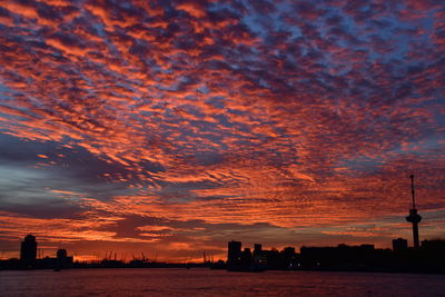 Silhouette of city against cloudy sky during sunset