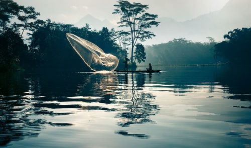 Fisherman throwing fishing net from boat in river during sunrise