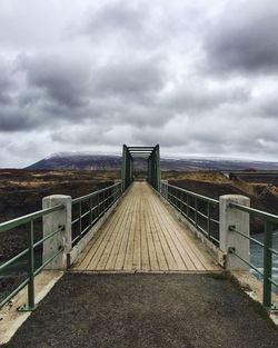 Footbridge over sea against cloudy sky