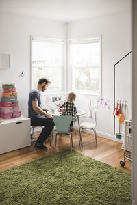 Father playing with daughter at small dining table in playroom