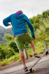 Rear view of man skateboarding against sky