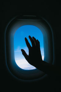 Close-up of silhouette hand against sky seen through airplane window