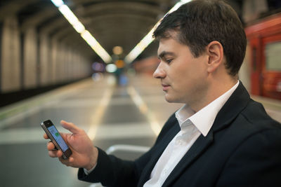 Side view of businessman using smart phone while sitting at subway station
