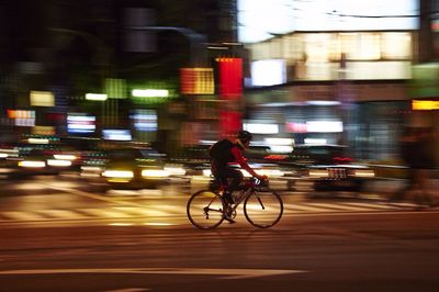 Side view of man bicycling on road against blurred cars