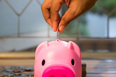 Cropped hand of man putting coin in piggy bank on table