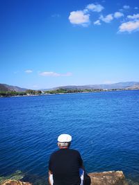 Rear view of man looking at sea against blue sky