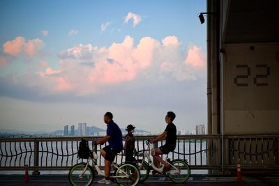 People riding bicycle on bridge against sky during sunset