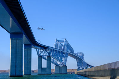 Low angle view of bridge over river against clear blue sky