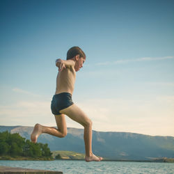 Full length of shirtless boy jumping in sea